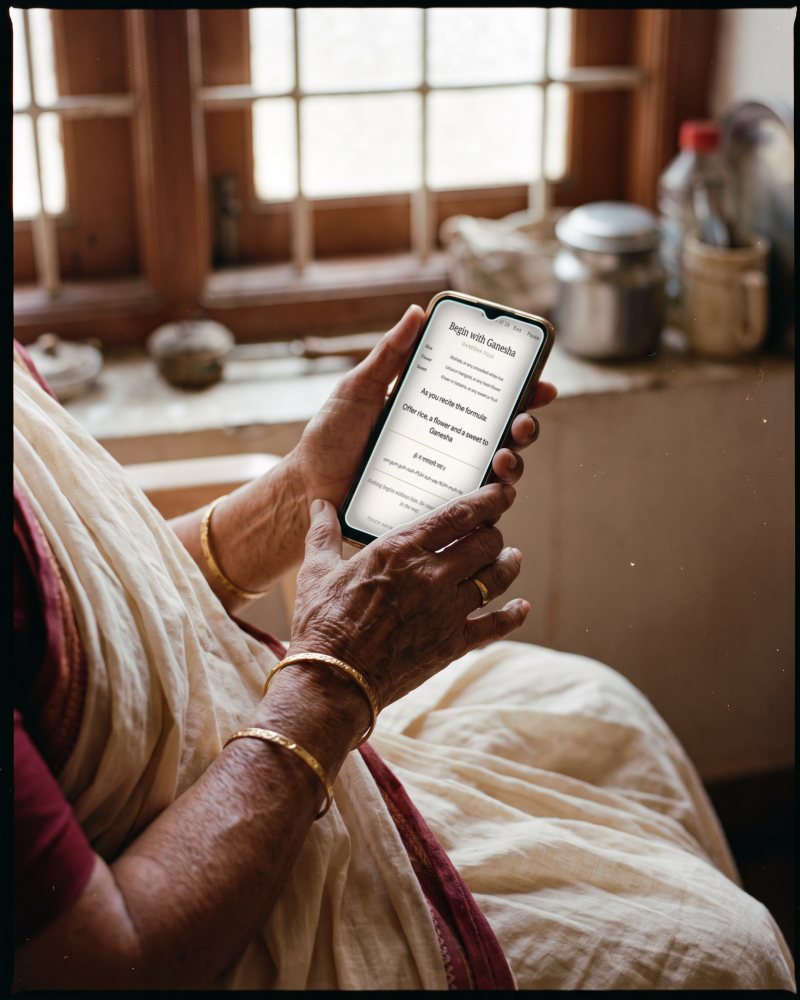 An elderly woman's hands holding a phone showing a step of the rite, in morning light