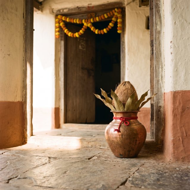 A copper kalash topped with mango leaves and a coconut at a doorway, marigolds strung above